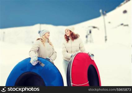 winter, leisure, sport, friendship and people concept - happy girl friends with snow tubes outdoors over mountain background