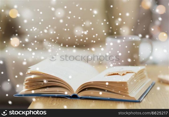 winter, literature and reading concept - open book with autumn leaf on wooden table at home over snow. book with autumn leaf on table over snow