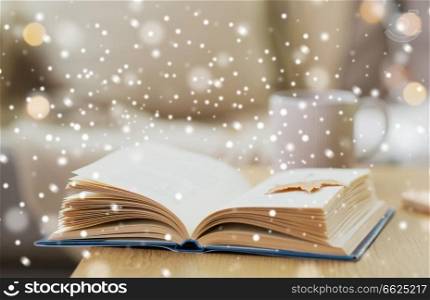 winter, literature and reading concept - open book with autumn leaf on wooden table at home over snow. book with autumn leaf on table over snow