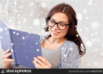 winter, literature, education and people concept - young woman in glasses reading book at home over snow