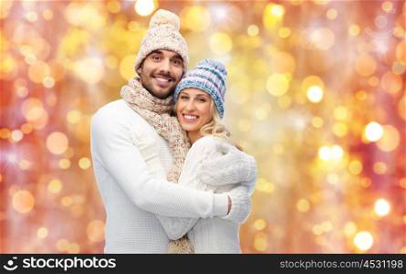 winter, love, couple, christmas and people concept - smiling man and woman in hats and scarf hugging over lights background