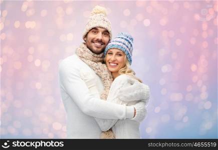 winter, love, couple, christmas and people concept - smiling man and woman in hats and scarf hugging over rose quartz and serenity lights background