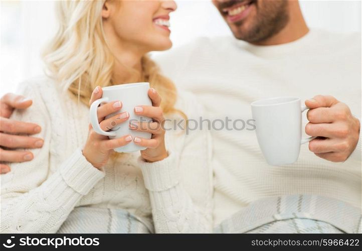 winter, love, family and happiness concept - close up of happy couple with tea cups at home