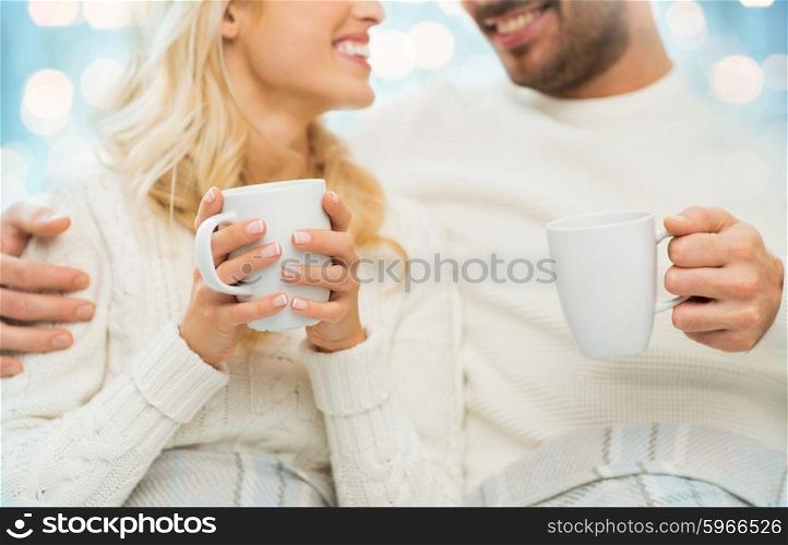 winter, love, family and happiness concept - close up of happy couple with tea cups at home over blue lights background