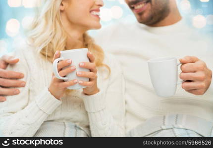 winter, love, family and happiness concept - close up of happy couple with tea cups at home over blue lights background