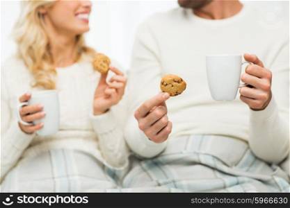 winter, love, food and sweets concept - close up of happy couple with oat cookies and tea cups at home
