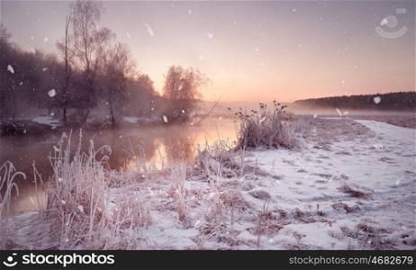 Winter misty dawn on the river. Snowflakes, snowfall. Sunny winter morning. Rural foggy frosty scene