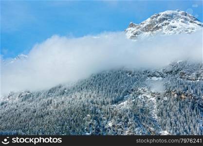 Winter mountain landscape with fir forest on slope and cloud (Austria, Tirol)