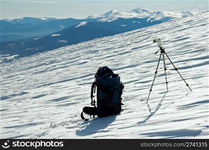 Winter mountain landscape with tourist knapsack and photographic tripod (Ukraine, Carpathian Mt&rsquo;s, Goverla and Petros Mountains behind)