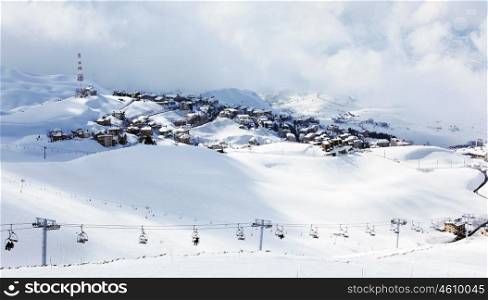 Winter mountain ski resort landscape with snow and cute little houses, chairlift with people playing sport