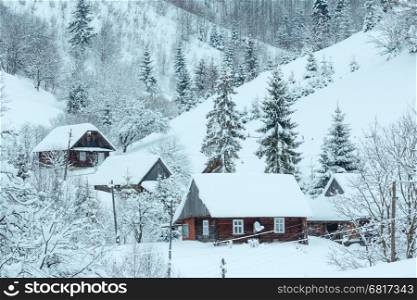 Winter mountain village. Wooden houses and fir trees on slope of Ukrainian Carpathian Mountains.