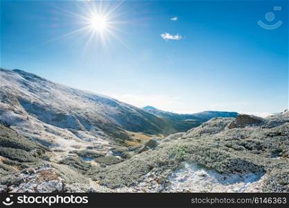 Winter mountains and sunny green valley beneath them. Landscape hills and bright sun