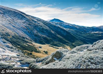 Winter mountains and sunny green valley beneath them. Landscape with peaks and snow