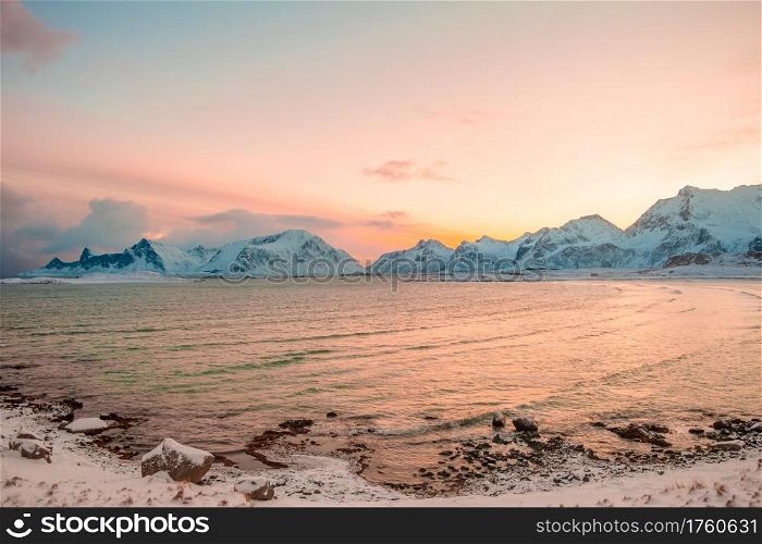 Winter. Norwegian fjord surrounded by snow-capped mountains in the early morning. Pink sky from rising sun reflected in water. Pink Morning over the Winter Fjord