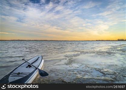 winter paddling - stand up paddleboard on an icy shore of Boyd Lake in northern Coplorado