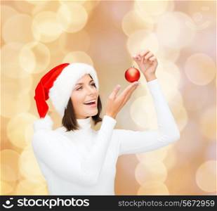 winter, people, christmas and happiness concept - woman in santa helper hat with christmas tree decoration ball over beige lights background