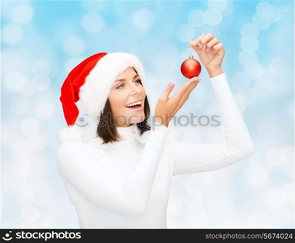 winter, people, christmas and happiness concept - woman in santa helper hat with christmas tree decoration ball over blue lights background