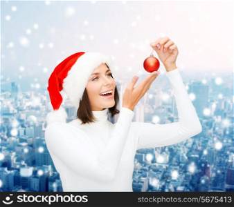 winter, people, christmas and happiness concept - woman in santa helper hat with christmas tree decoration ball over snowy city background