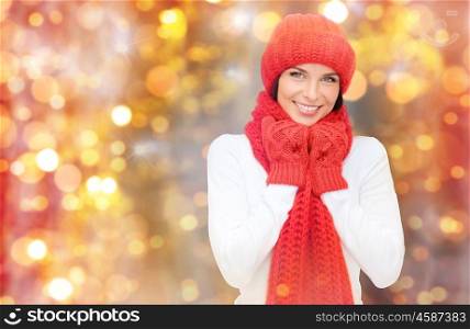 winter, people, christmas and holidays concept - happy smiling woman in hat, muffler and mittens over lights background