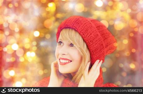winter, people, christmas and holidays concept - happy smiling woman in red hat and scarf over lights background