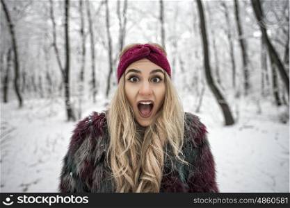 Winter portrait of excited woman posing in the snowy forest wearing a warm fur jacket