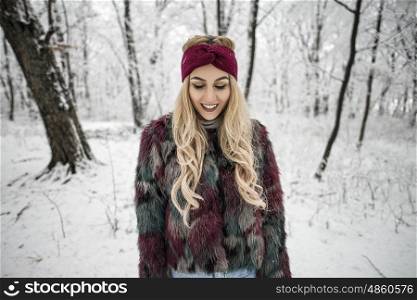 Winter portrait of happy woman posing in the snowy forest wearing a warm fur jacket