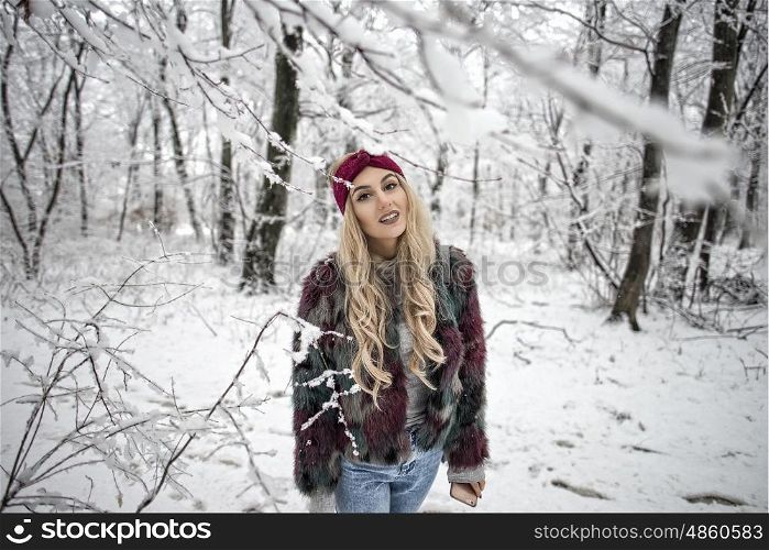 Winter portrait of woman posing in the snowy forest wearing a warm fur jacket