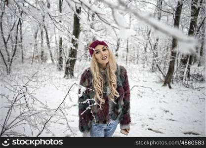Winter portrait of woman posing in the snowy forest wearing a warm fur jacket