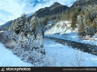 Winter river with snowy bushes and trees on bank.