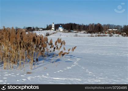Winter rural landscape with frozen river and dry reeds on the shore, sunny day