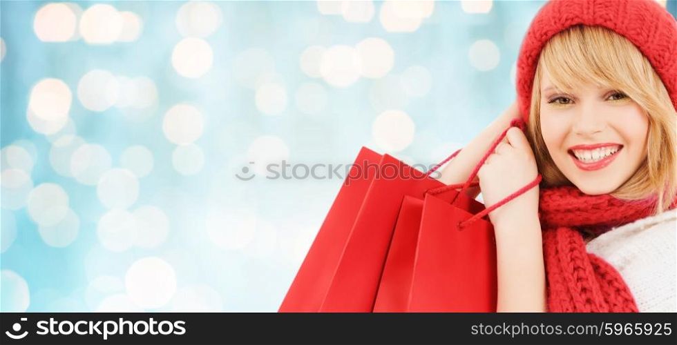 winter, sale, people and holidays concept - woman in red hat and scarf with many shopping bags over blue lights background