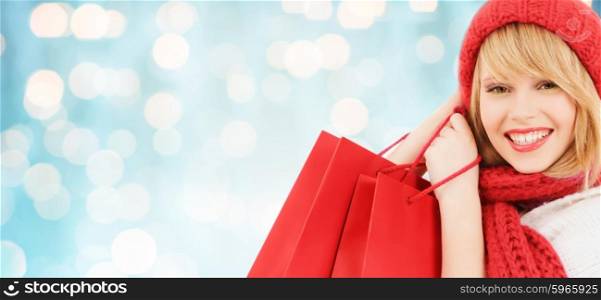 winter, sale, people and holidays concept - woman in red hat and scarf with many shopping bags over blue lights background