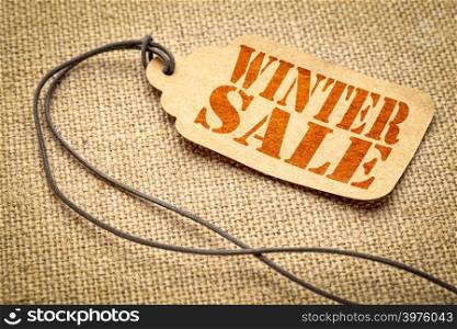 winter sale sign - red stencil text on a paper price tag against burlap canvas