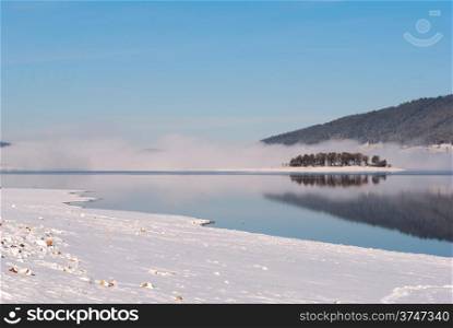 Winter scene of a lake, small island and forest, fog