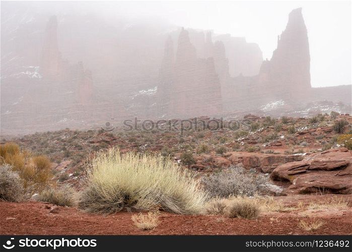 winter scenery of southwest landscape with falling snow and fog - Fisher Towers in the Moab area in Utah
