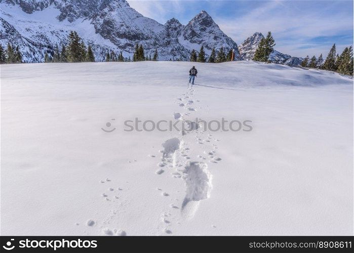 Winter scenery with a man walking through snow on a mountain peak, leaving a trail of footsteps behind him. Picture taken on Austrian Alps, near Ehrwald resort.
