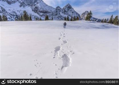 Winter scenery with a man walking through snow on a mountain peak, leaving a trail of footsteps behind him. Picture taken on Austrian Alps, near Ehrwald resort.