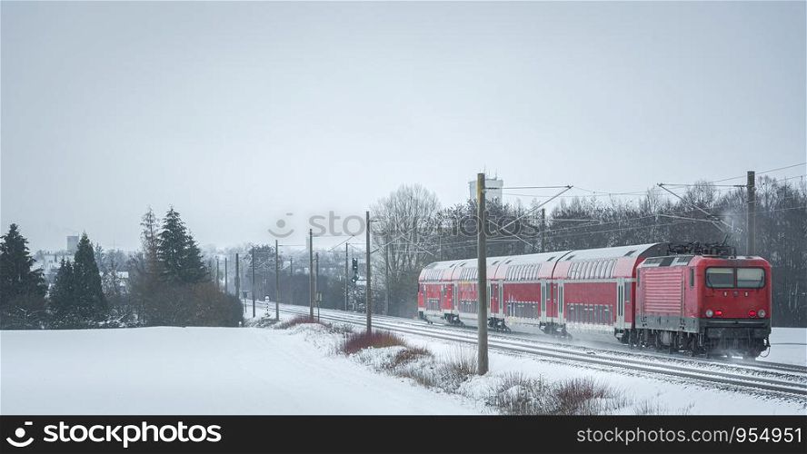 Winter scenery with a passenger train on the snowy railroad. Red train traveling in a winter decor