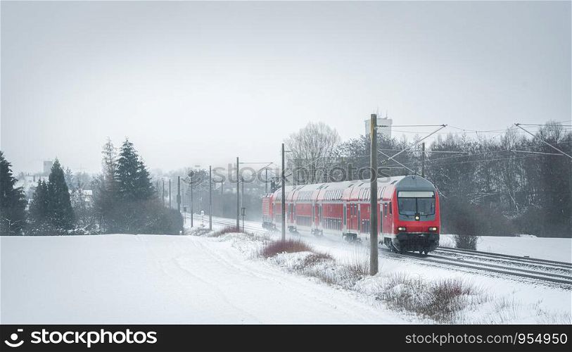 Winter scenery with a red train traveling near a village. Passengers train on the snowy railroad.