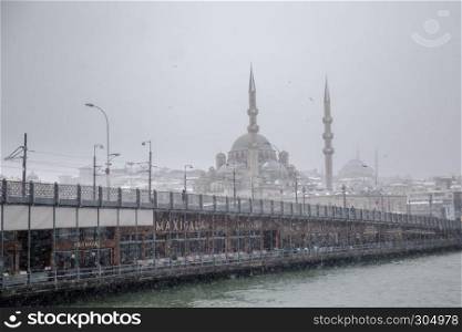 Winter seascape view of Popular New Mosgue and Galata Bridge.Seagulls flying over bosphorus on a snowy day in winter.. Winter seascape view of Popular New Mosgue and Galata Bridge