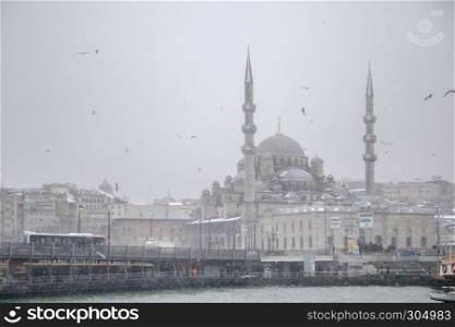 Winter seascape view of Popular New Mosgue and Galata Bridge.Seagulls flying over bosphorus on a snowy day in winter.. Winter seascape view of Popular New Mosgue and Galata Bridge