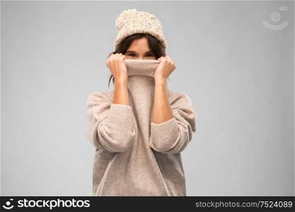 winter season and people concept - happy young woman in knitted hat covering face with warm sweater over grey background. young woman in knitted winter sweater and hat