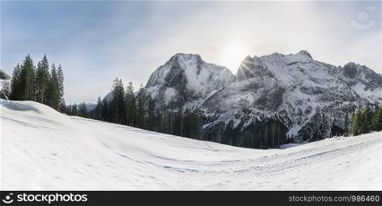 Winter snow panorama with snowdrifts, majestic snowy Alps mountains and fir forest, in Ehrwald, Austria. Sunshine in the mountains. Winter wonderland