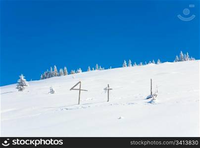 winter snowy fir trees on mountainside on blue sky background and wooden cross in front (Carpathians, Ukraine)