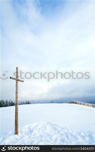 winter snowy fir trees on mountainside on overcast sky background and wooden cross in front (Carpathians, Ukraine)