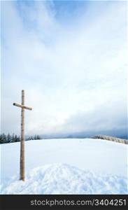 winter snowy fir trees on mountainside on overcast sky background and wooden cross in front (Carpathians, Ukraine)
