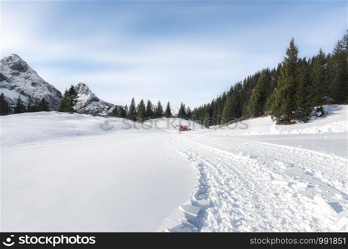 Winter snowy landscape with snow-capped Alps mountains peaks, fir forest, and snow-covered fresh road. Snowmobile tracks snow road. Ehrwald, Austria.