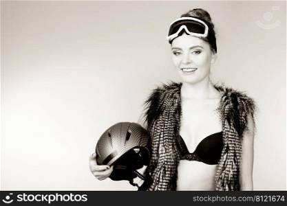 Winter sport activity concept. Atractive smiling woman wearing bra, ski goggles and furry waistcoat holding helmet, black and white.. Woman wearing sexy winter sport outfit