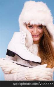 Winter sport activity concept. Girl wearing furry hat and warm clothes holding and hugging ice skate, blue background studio shot.. Woman wearing winter hat hugging ice skate