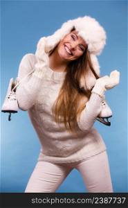 Winter sport activity concept. Girl wearing furry hat and warm clothes holding ice skate, blue background studio shot.. Woman wearing winter hat holding ice skate